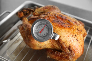 Golden roasted turkey on baking tray with a meat thermometer