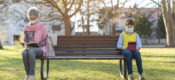 Grandmother and grandson separated by social distancing sitting on park bench