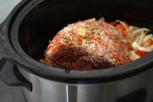 Roasted Leg of Lamb food preparation cooking in a slow cooker with vegetables and herbs.