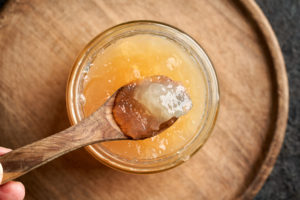 Cooled congealed beef bone broth on a wooden spoon above a glass jar